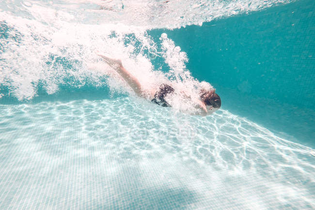 Menino em calções de banho mergulhando na água da piscina azul transparente — Fotografia de Stock