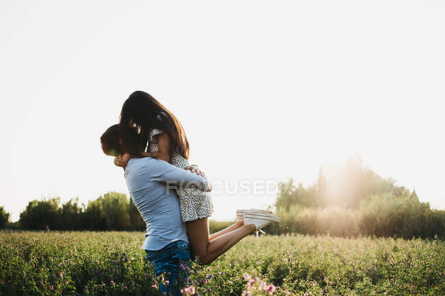 Vista lateral de un hombre y una mujer irreconocibles abrazándose y abrazándose en el campo con retroiluminación - foto de stock