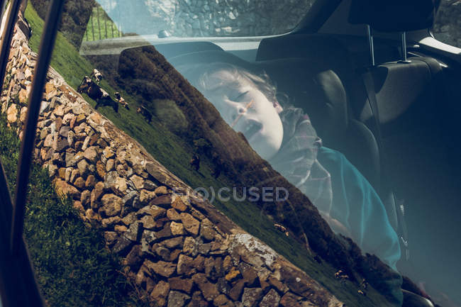 Mignon jeune garçon assis et dormant dans la voiture garée dans la nature . — Photo de stock