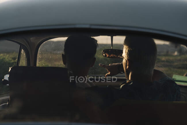 Vista posteriore di due giovani uomini irriconoscibili che abbracciano e ammirano la natura seduti all'interno di un'auto retrò — Foto stock
