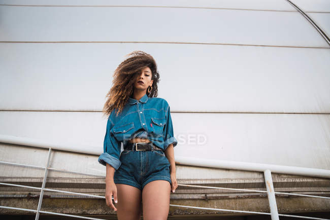 Young african american woman in denim clothes standing at balcony near railing — Stock Photo