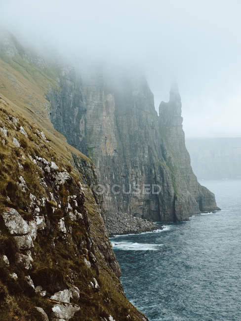 Océano y acantilado rocoso en las nubes en la isla de Feroe - foto de stock