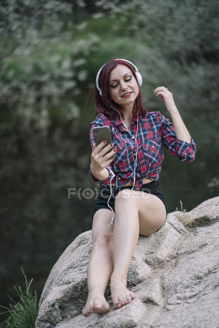 Chica pelirroja escucha música junto al río - foto de stock