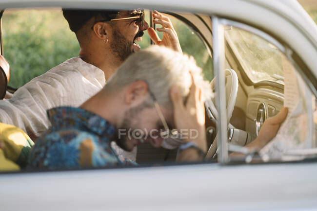 Two young guys laughing and holding map while sitting inside retro car during nice travel — Stock Photo