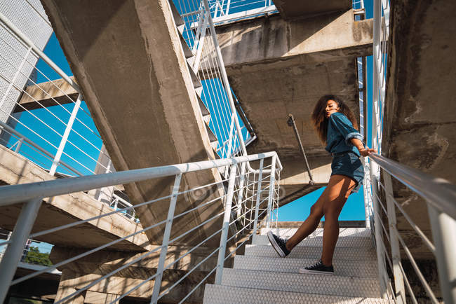 Young woman in denim clothes leaning on railing of staircase — Stock Photo