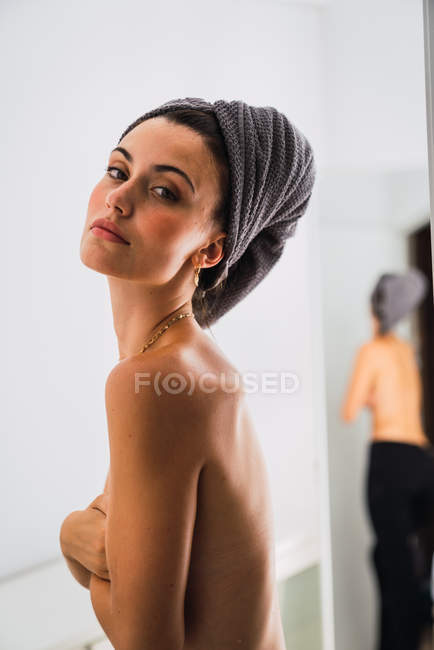 Jeune femme sensuelle seins nus debout devant le miroir avec une serviette sur la tête — Photo de stock