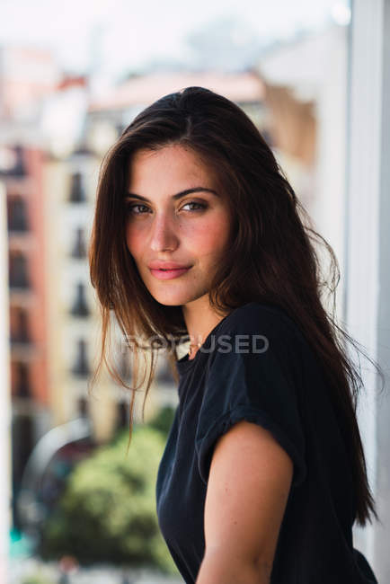 Молодая улыбающаяся женщина стоит на балконе и смотрит в камеру — стоковое фото