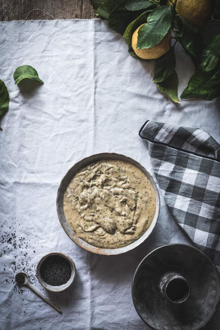 From above view of gravy in dish near cup of poppy seed and lemon branch on white wrinkled cloth — Stock Photo