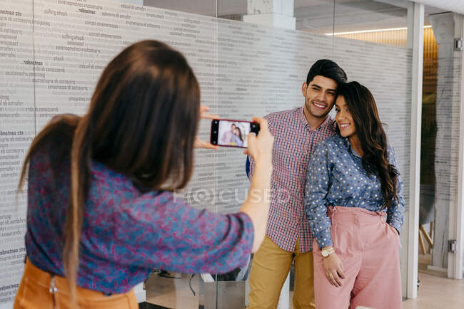 Задний вид женщины стоящей и фотографирующей людей в офисе со смартфоном. — стоковое фото