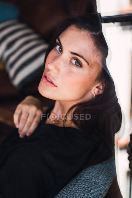 Young brunette woman sitting in armchair and looking at camera — Stock Photo