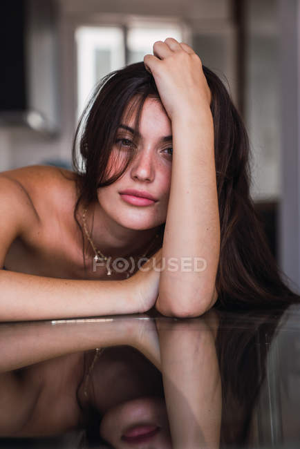 Mujer sensual joven apoyada en mesa de cristal con la mano en el pelo - foto de stock