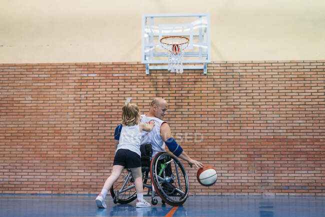 Спортивные мужчины и девочки с ограниченными возможностями во время игры в баскетбол в помещении — стоковое фото