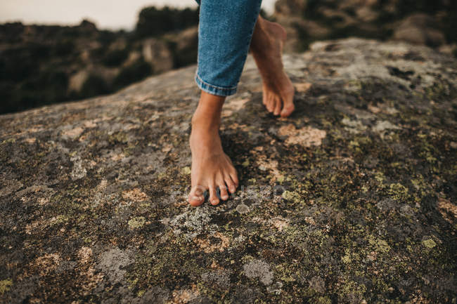 Cropped image of barefoot woman in jeans walking on rock — стокове фото