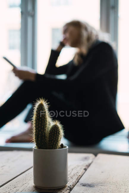 Potted cactus on wooden table with woman reading book on background — Stock Photo