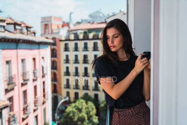 Mujer joven de pie en el balcón con cámara de fotos en la ciudad vieja - foto de stock