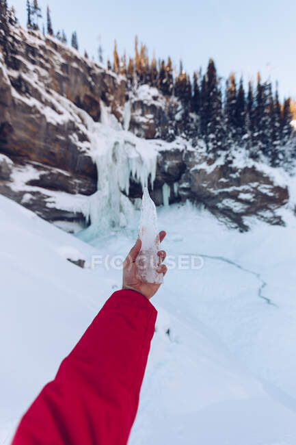 Crop hand in red winter jacket holding piece of crystal ice on background of mountains in snow, Canada — Stock Photo