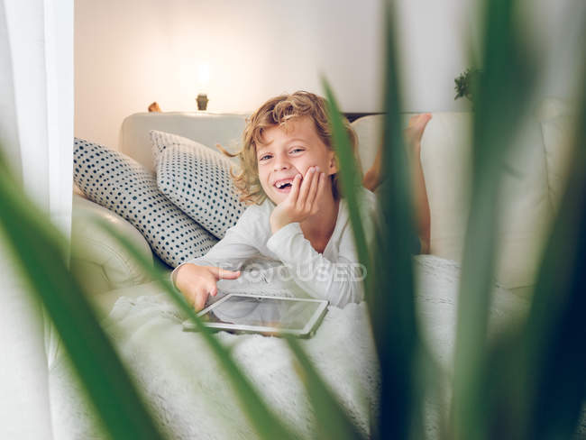 Смеющийся мальчик с планшета на диване дома — стоковое фото