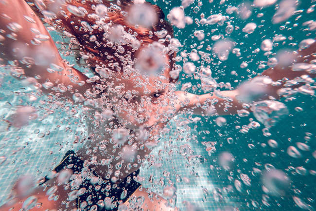 Kid diving in water with air bubbles against background of transparent water — Stock Photo