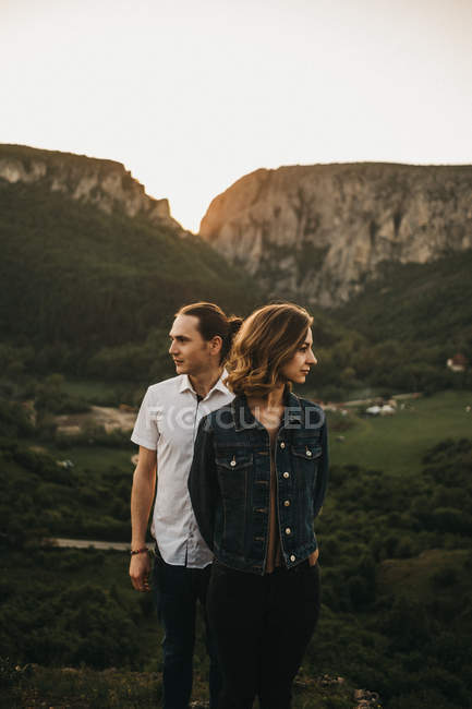 Hombre y mujer mirando hacia otro lado mientras están de pie sobre el fondo de increíbles montañas y valle juntos - foto de stock