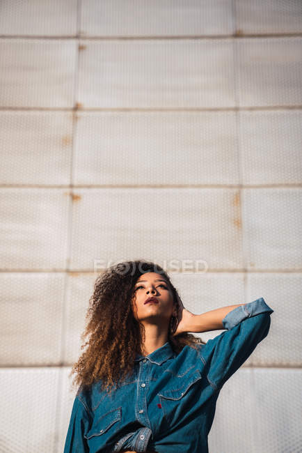 Junge Frau in Jeanshemd steht vor Wand und schaut auf — Stockfoto