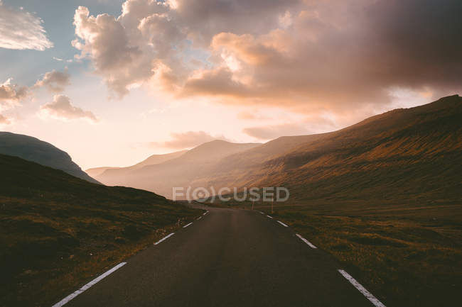 Vista prospectiva da estrada de asfalto entre colinas em luzes de pôr do sol nas Ilhas Feroé — Fotografia de Stock