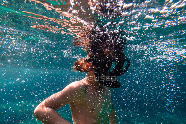 Niño anónimo en máscara de buceo snorkeling en agua burbujeante de mar azul - foto de stock