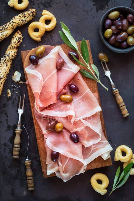 Jambon de prosciutto aux olives sur planche à découper en bois — Photo de stock