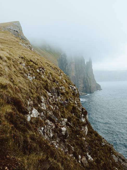 Océan et falaise rocheuse dans les nuages sur l'île Feroe — Photo de stock