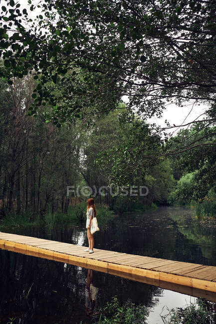 Jeune femme marchant sur le pont sur la rivière — Photo de stock