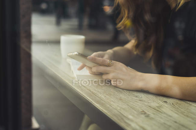 Primo piano della donna utilizzando smartphone nel bar dietro il vetro della finestra — Foto stock