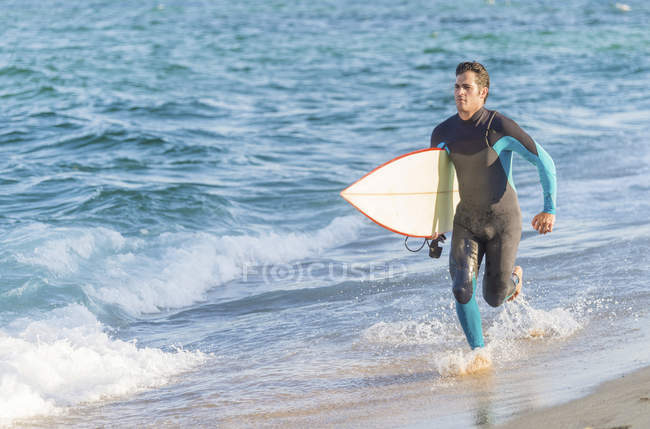 Hombre haciendo un poco de correr en la playa antes de surfear
. - foto de stock
