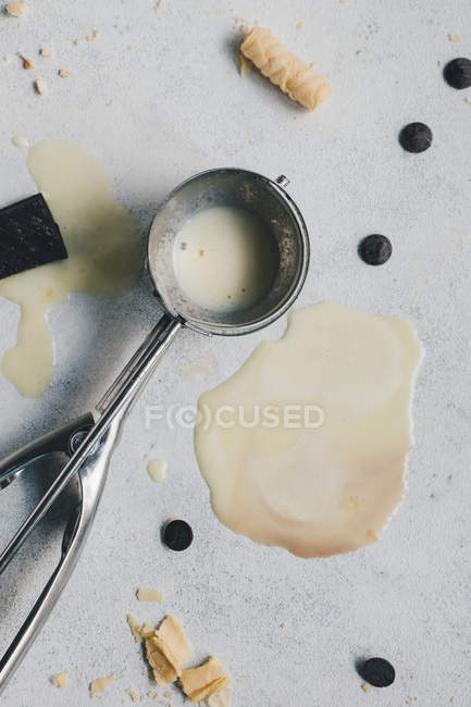 Helado de vainilla derretido y cuchara de plata en superficie blanca - foto de stock