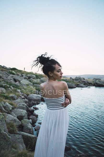 Mujer joven en vestido elegante de pie cerca del lago ondulante - foto de stock