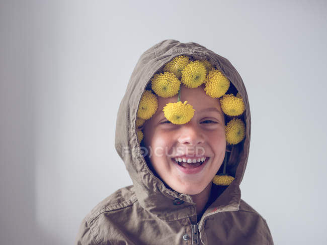 Porträt eines fröhlichen Jungen mit Blumen in Kapuze auf weißem Hintergrund — Stockfoto