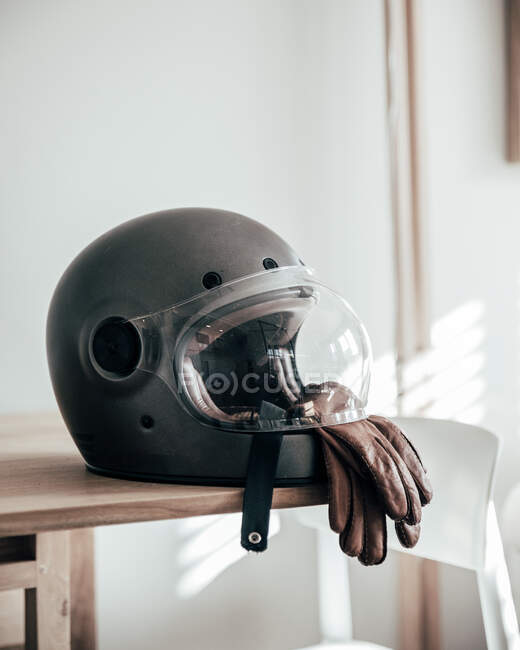 Крупный план мотоциклетного шлема и кожаных перчаток лежащих на столе в стильной комнате — стоковое фото