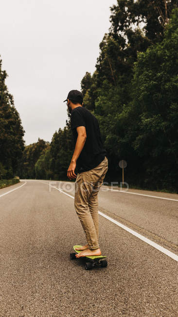Hombre descalzo skateboarding a lo largo de la carretera - foto de stock