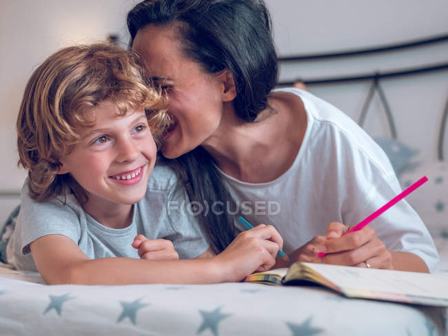 Красива жінка і мила дитина лежить на зручному ліжку і розмальовує картинки в блокноті разом — стокове фото