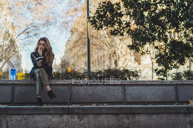 Jeune femme lecture livre sur escalier dans le parc de la ville — Photo de stock