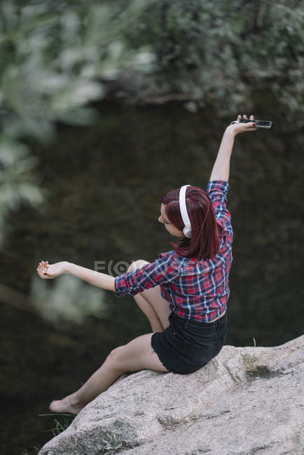 Chica pelirroja escucha música junto al río - foto de stock
