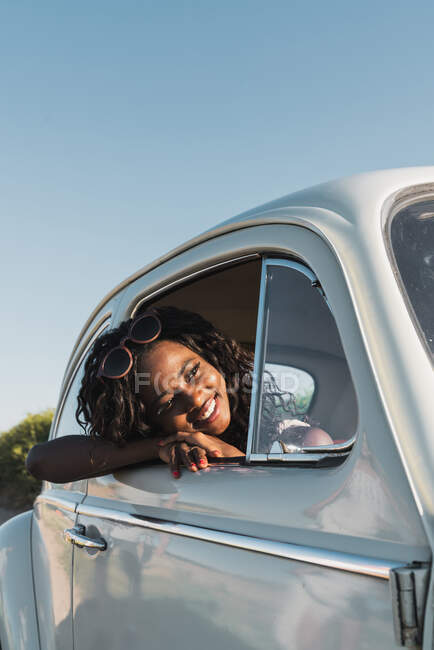 Happy young black woman in stylish sunglasses looking out of car window enjoying summer sunlight — Stock Photo