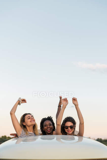 Grupo de jovens amigos diversos que estão na escotilha no telhado da van vintage e olhando para a câmera enquanto passam o tempo na natureza juntos — Fotografia de Stock