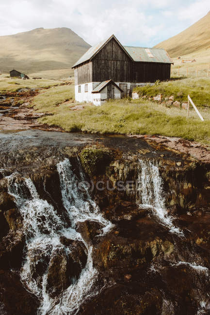 Wasserfall und ländliches Holzhaus am Hang auf Feroe Islands — Stockfoto