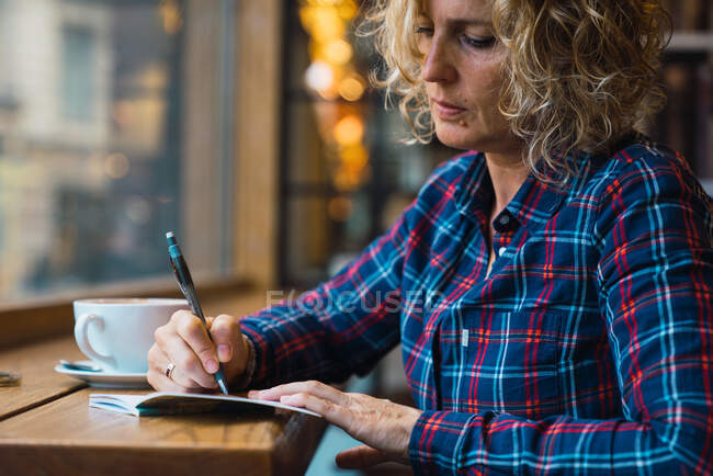 Femme assise dans un café et écrivant dans un cahier — Photo de stock