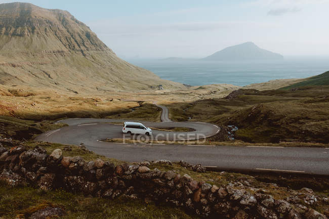 Coche blanco que conduce en la carretera serpentina en las montañas en las Islas Feroe - foto de stock