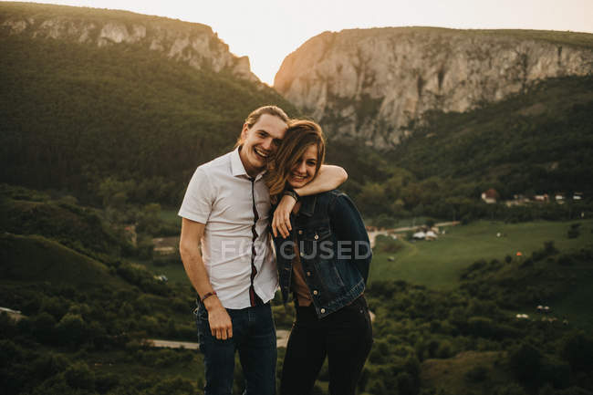 Милая пара обнимает и выносливые лбы, стоя на фоне красивой долины и гор — стоковое фото