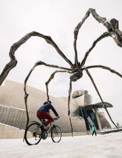 Bicyclist riding under modern monument in winter — Stock Photo