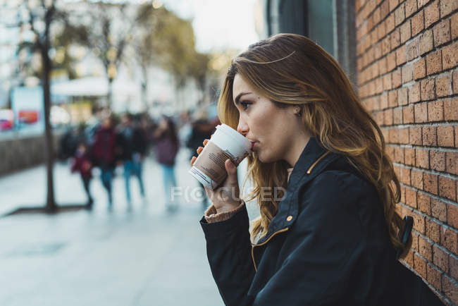 Молодая женщина с бумажной чашкой кофе стоит на улице — стоковое фото