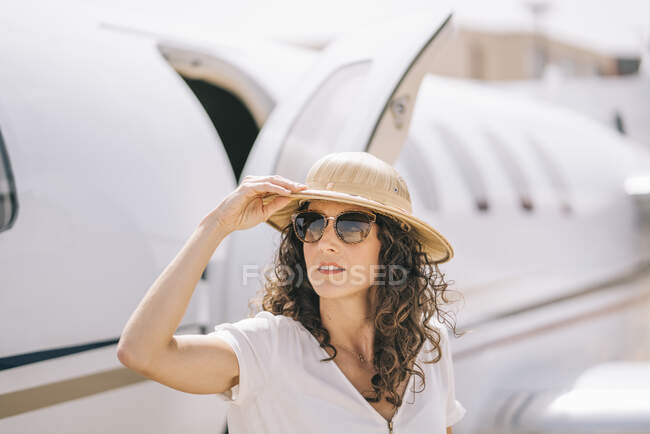 Hübsche Frau mit Sonnenbrille und Hut neben einem Flugzeug. — Stockfoto