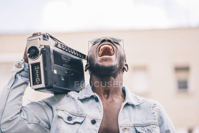 Sorrindo homem negro em óculos de sol andando com dispositivo de rádio vintage e cantando — Fotografia de Stock