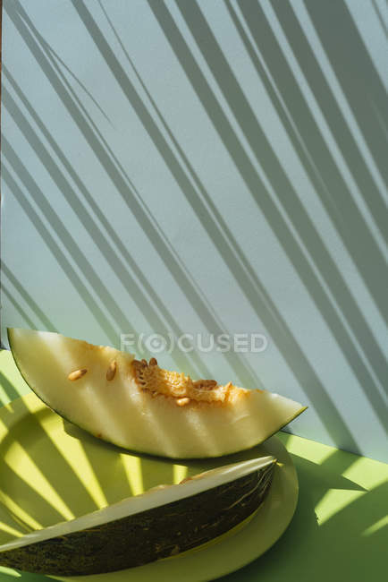 Скибочки свіжої дині на тарілці на синьо-зеленому фоні з тінями пальмового листя — стокове фото